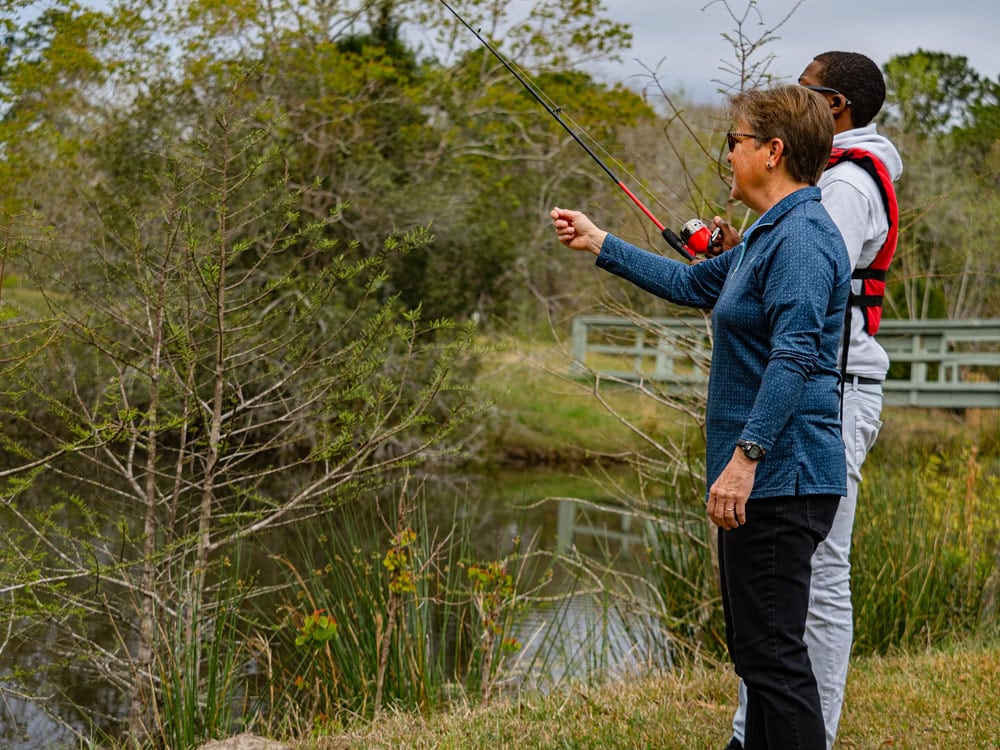 Female volunteer gesturing to a Windwood resident as he fishes at the pond