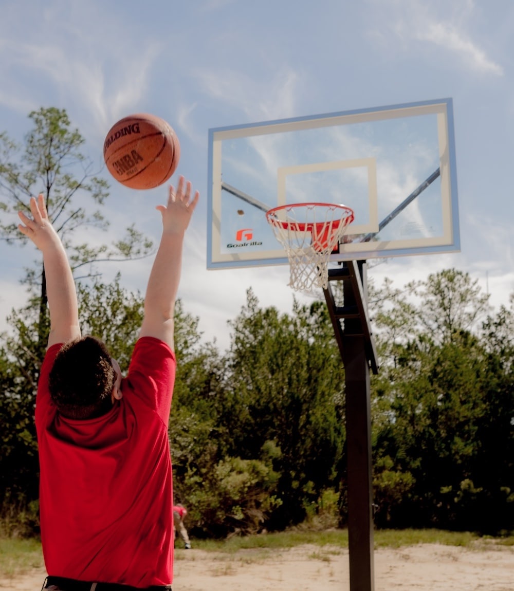 A teen boy shoots a basketball at Windwood's outside basketball hoop